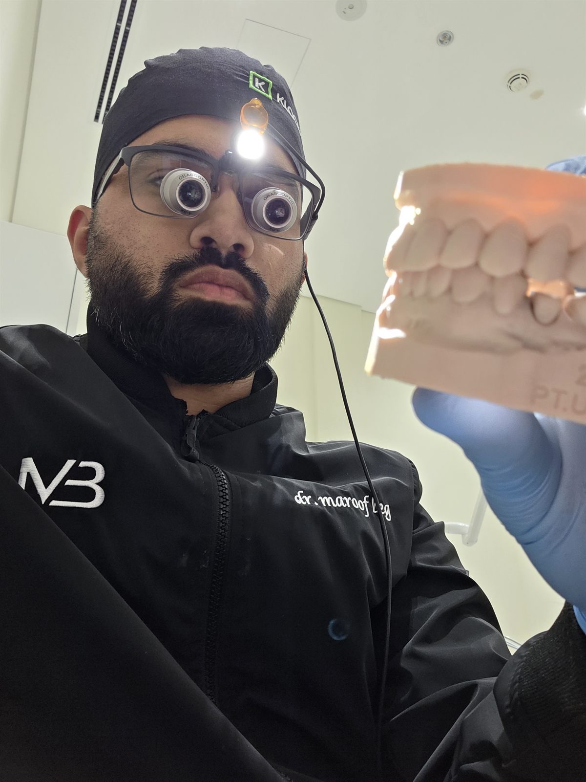 Dr. Maroof Beg wearing surgical loupes, closely examining a dental model to plan a case